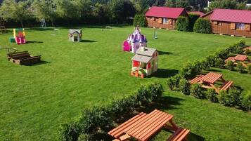 Un campo cubierto de césped con estructuras de juego, mesas de picnic y cabañas de madera.