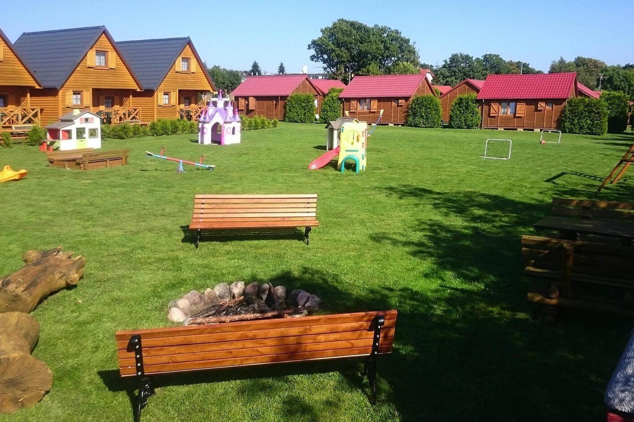 Un espacio al aire libre con césped, bancos de madera, una pequeña zona de juegos y un hogar para la chimenea.