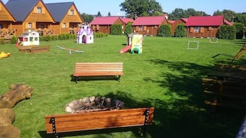 Un espacio al aire libre con césped, bancos de madera, una pequeña zona de juegos y un hogar para la chimenea.