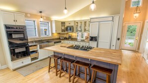 Uma cozinha moderna com ilha central, banquetas, forno embutido, micro-ondas e geladeira.
