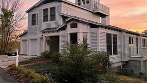 Uma casa moderna de dois andares, com varanda e uma pequena estrutura em formato de torre no telhado.