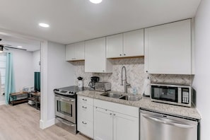 Une cuisine moderne avec des meubles blancs, un lave-vaisselle en acier inoxydable, un four à micro-ondes et une cuisinière à gaz.