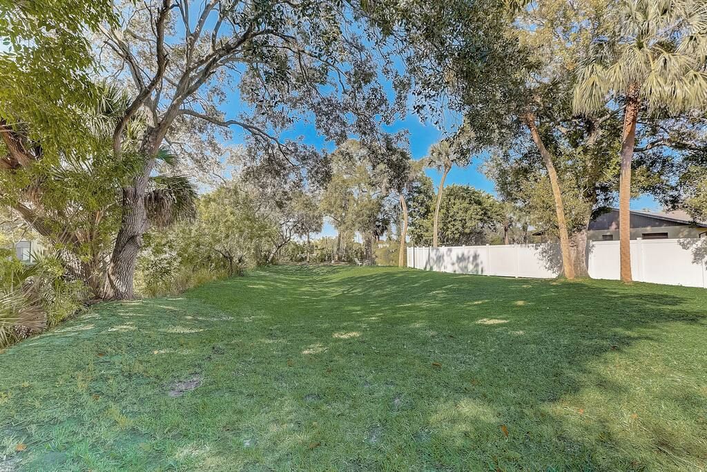 A well-maintained grassy yard with mature trees and a white fence.