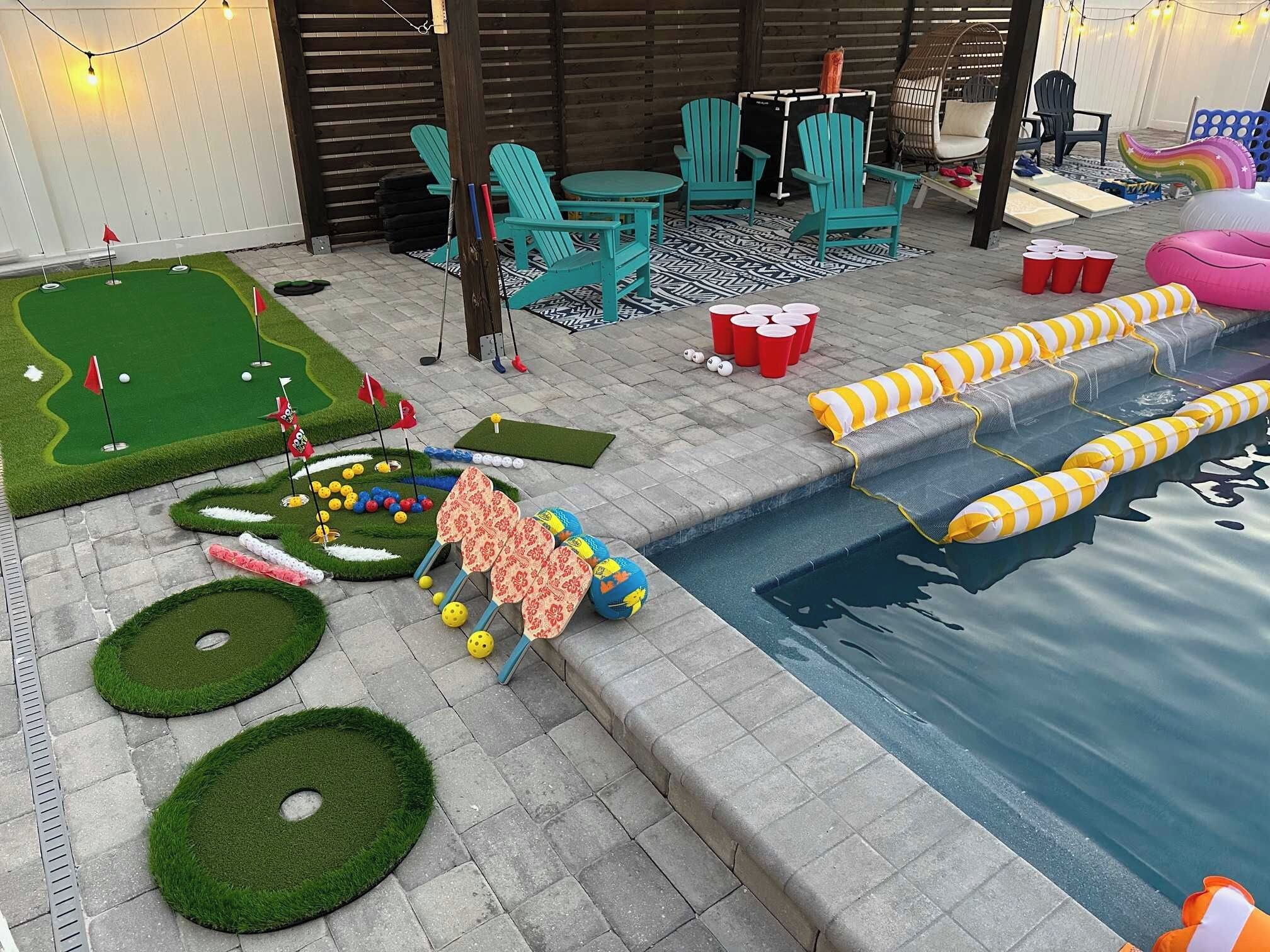 Area piscina con un piccolo campo da golf, sedie a sdraio e un tavolo a bordo piscina.