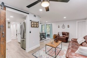 A modern living room with a large brown leather sofa, a wooden coffee table, and a sliding barn door leading to a kitchen.