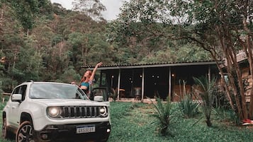 Um SUV branco estacionado em um jardim exuberante, com uma área coberta ao fundo.