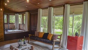 A cozy room with a wooden ceiling, a sofa with patterned cushions, a small table with a lantern, and a red cabinet. - Pousada irreplaceable (Bocaina de Minas)