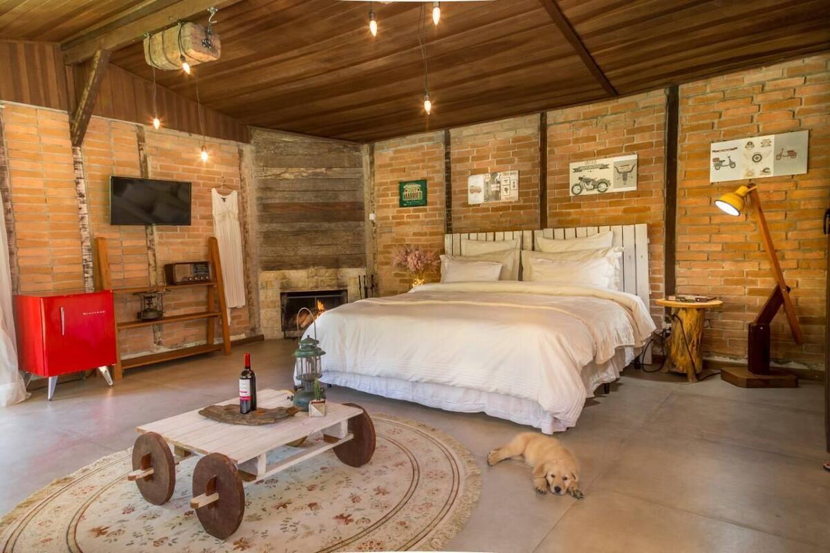 Un dormitorio rústico con pared de ladrillo, techo de madera, cama, un armario rojo, un televisor y un perro.