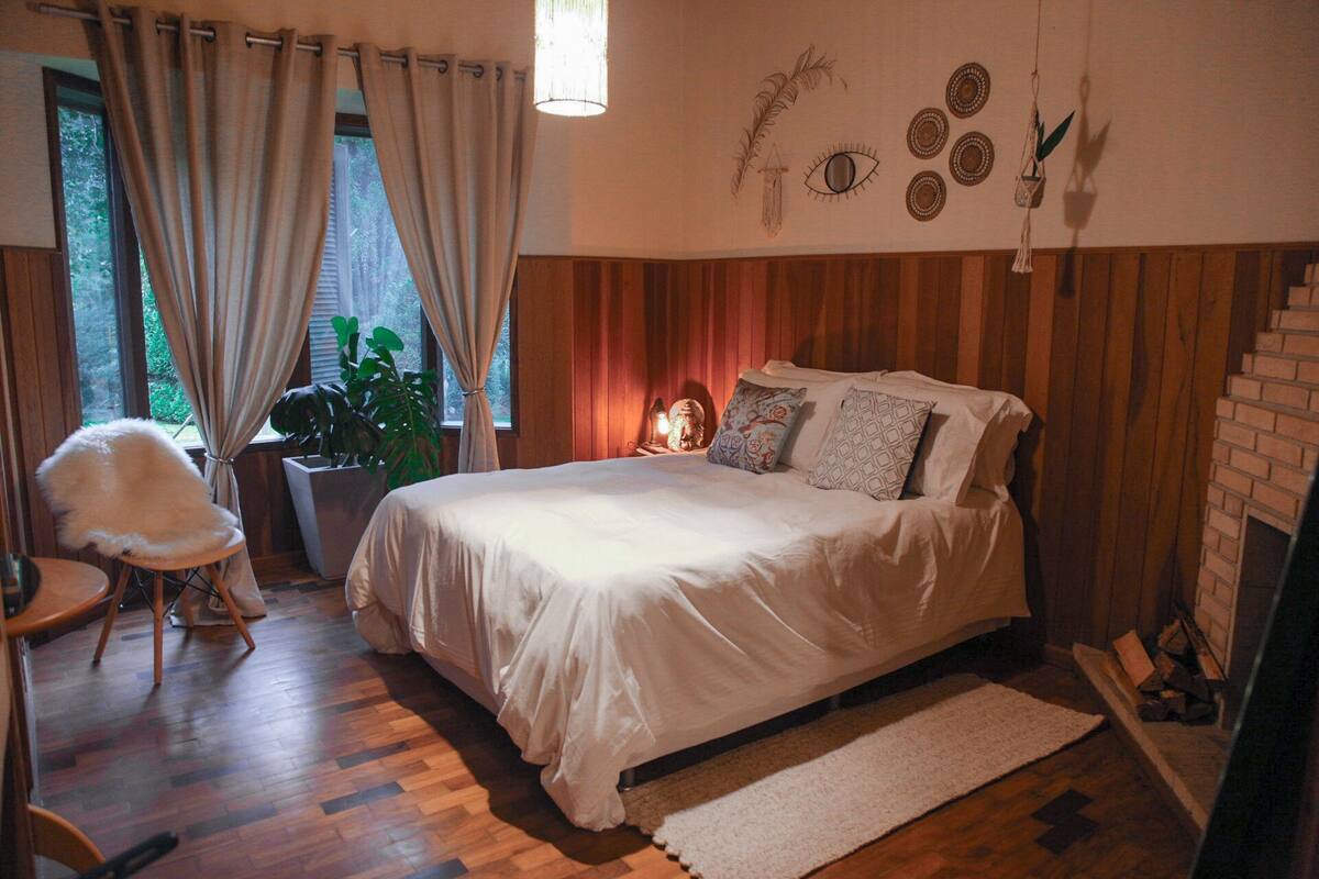 Un dormitorio acogedor con una cama grande, piso de madera, una planta en maceta y una chimenea.