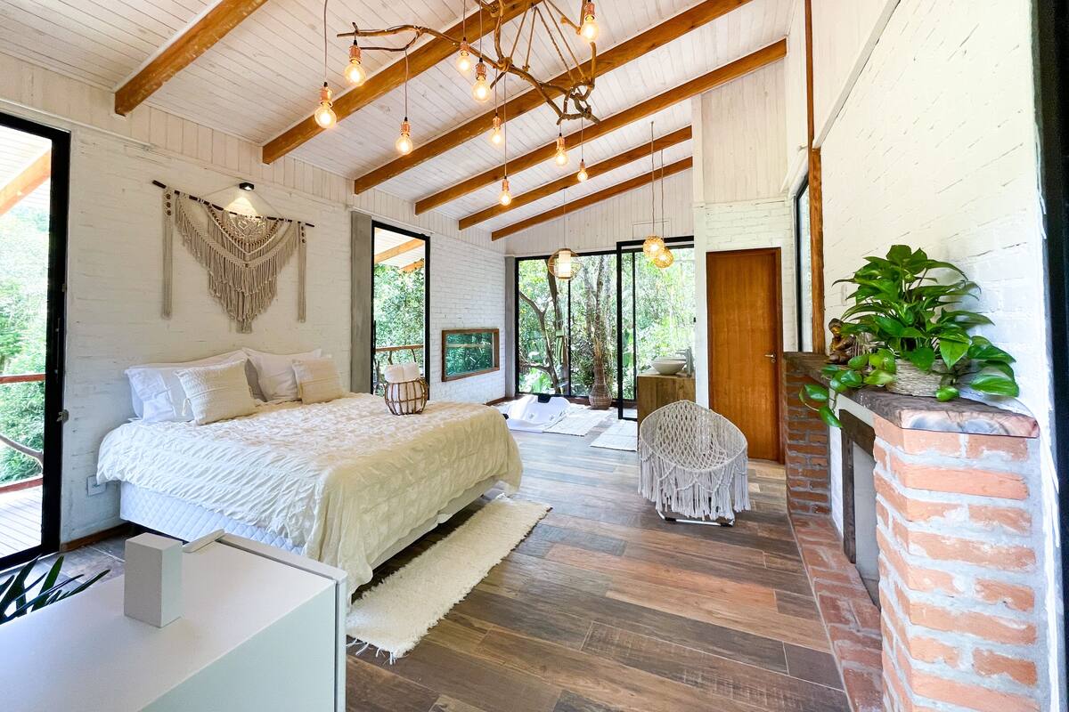 Un dormitorio con una cama, una pared blanca, un colgador de macramé y un techo de madera.