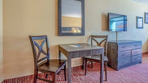 Habitación de hotel con un escritorio de madera, dos sillas, un espejo, un televisor y un aparador.