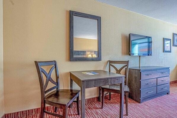 A hotel room with a wooden desk, two chairs, a mirror, a TV, and a dresser.