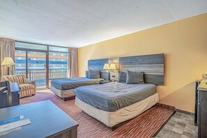 A hotel room with two beds, a desk, a chair, and a large window with a view of a building.