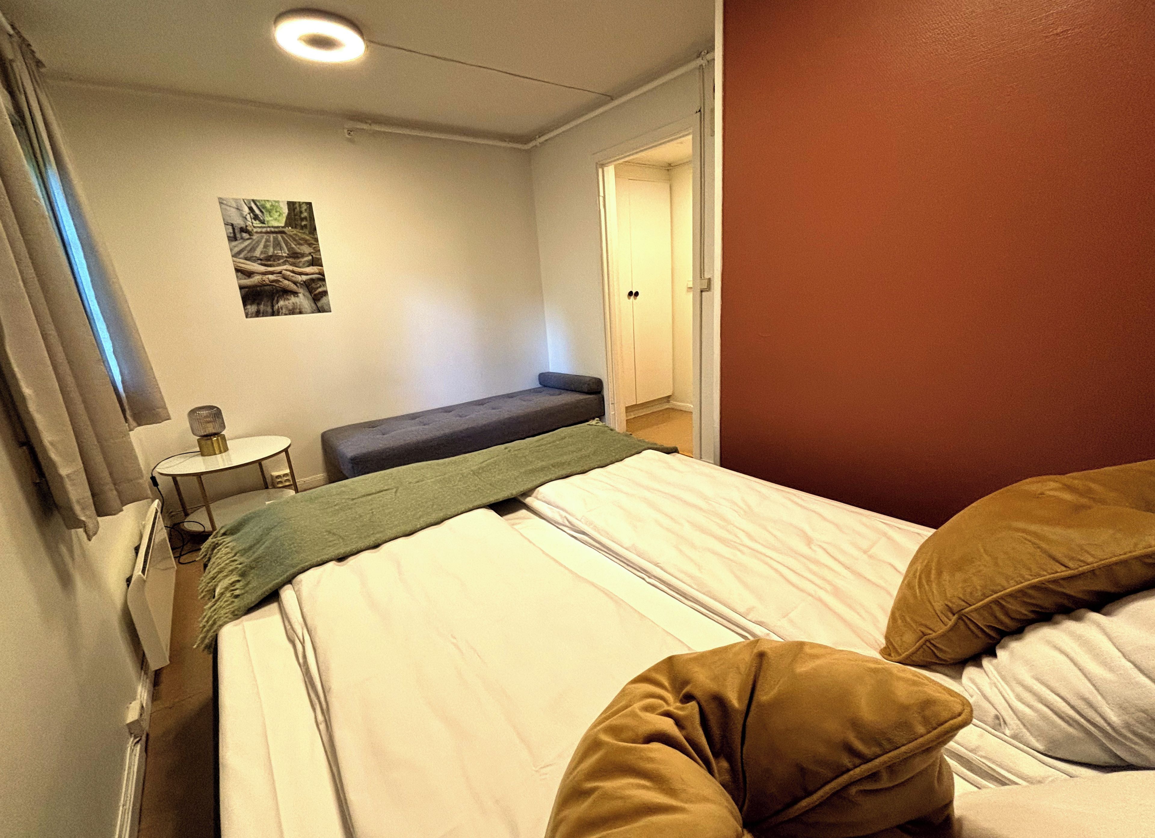 A hotel room with a bed, a bench, a small table, and a picture on the wall.