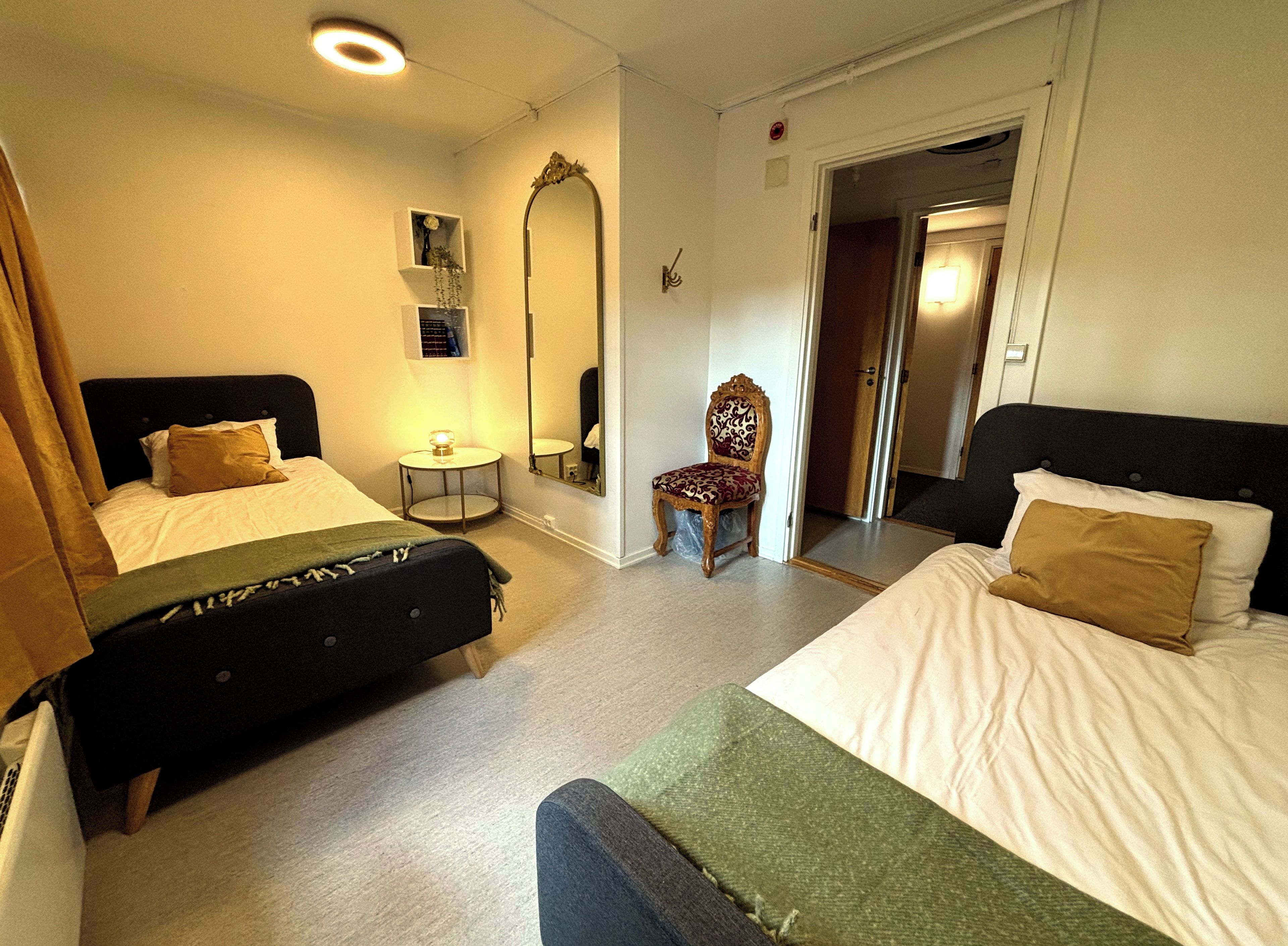 Habitación de hotel con dos camas, una silla, un espejo y una mesita.