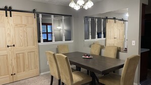 Un comedor con una mesa de madera oscura, sillas tapizadas en color beige y una araña.