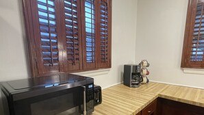 A kitchen with a microwave, coffee maker, wooden cabinets, and a window with blinds. - 11-Guests/Airport -Minute Away/Pet-Welcome/4-BDR/2-FBA/5-QBED! (Oklahoma City)