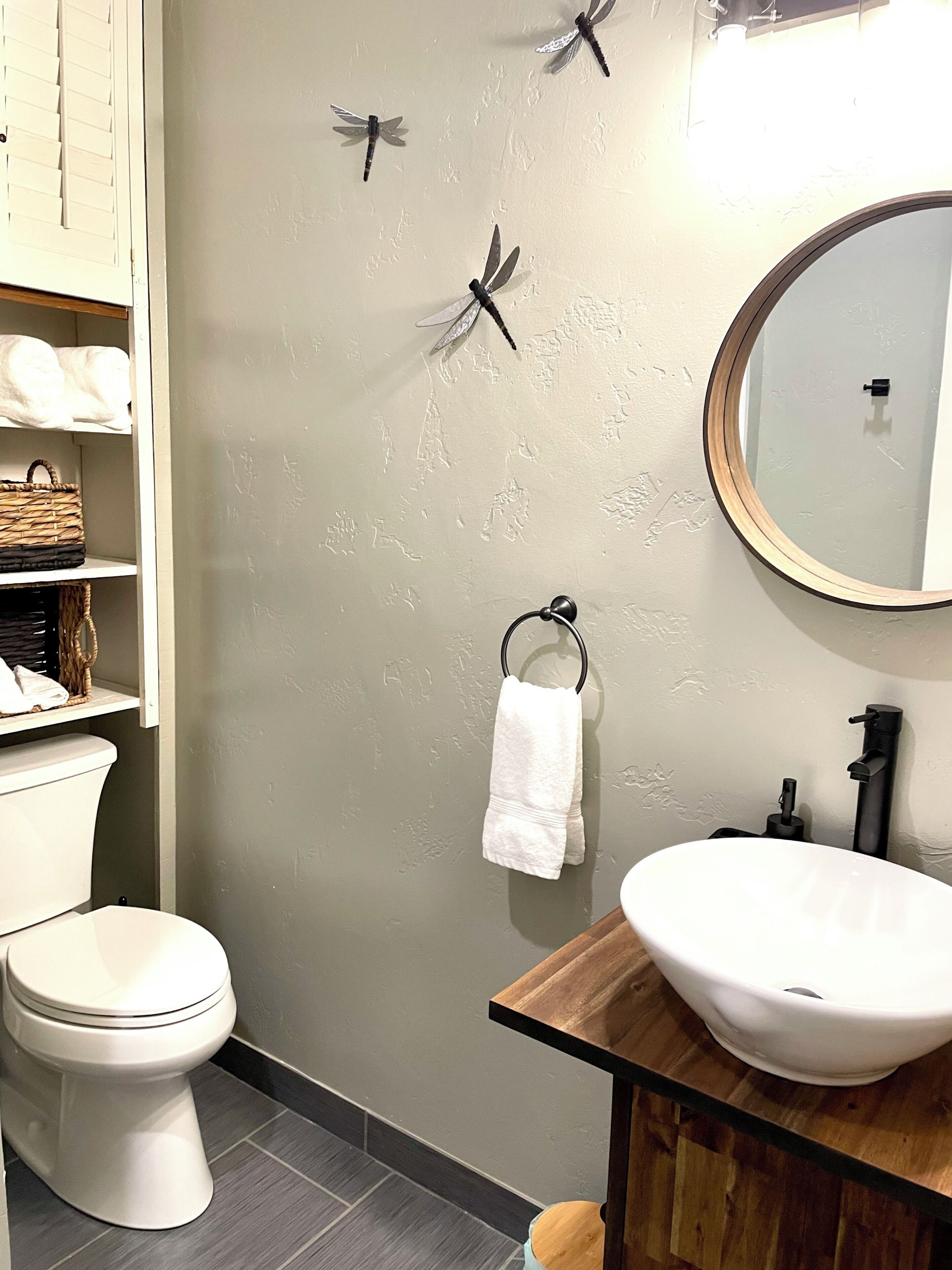 A bathroom with a toilet, a sink, a mirror, and decorative dragonfly wall art.