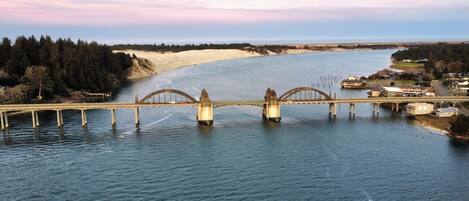 Un grand pont enjambant une large rivière, avec une rive bordée d’une forêt et une petite ville en arrière-plan.