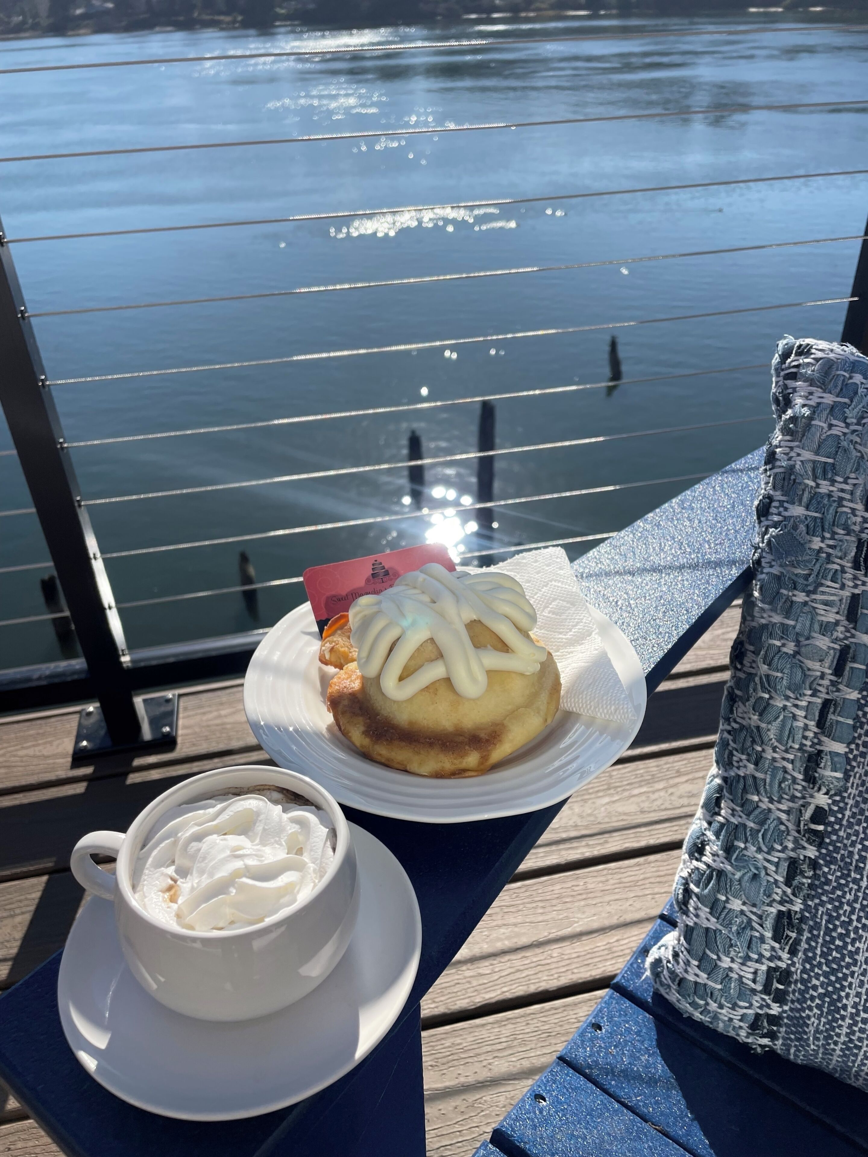 Una mesa con un plato de comida y una taza de café en una terraza con vista al agua.