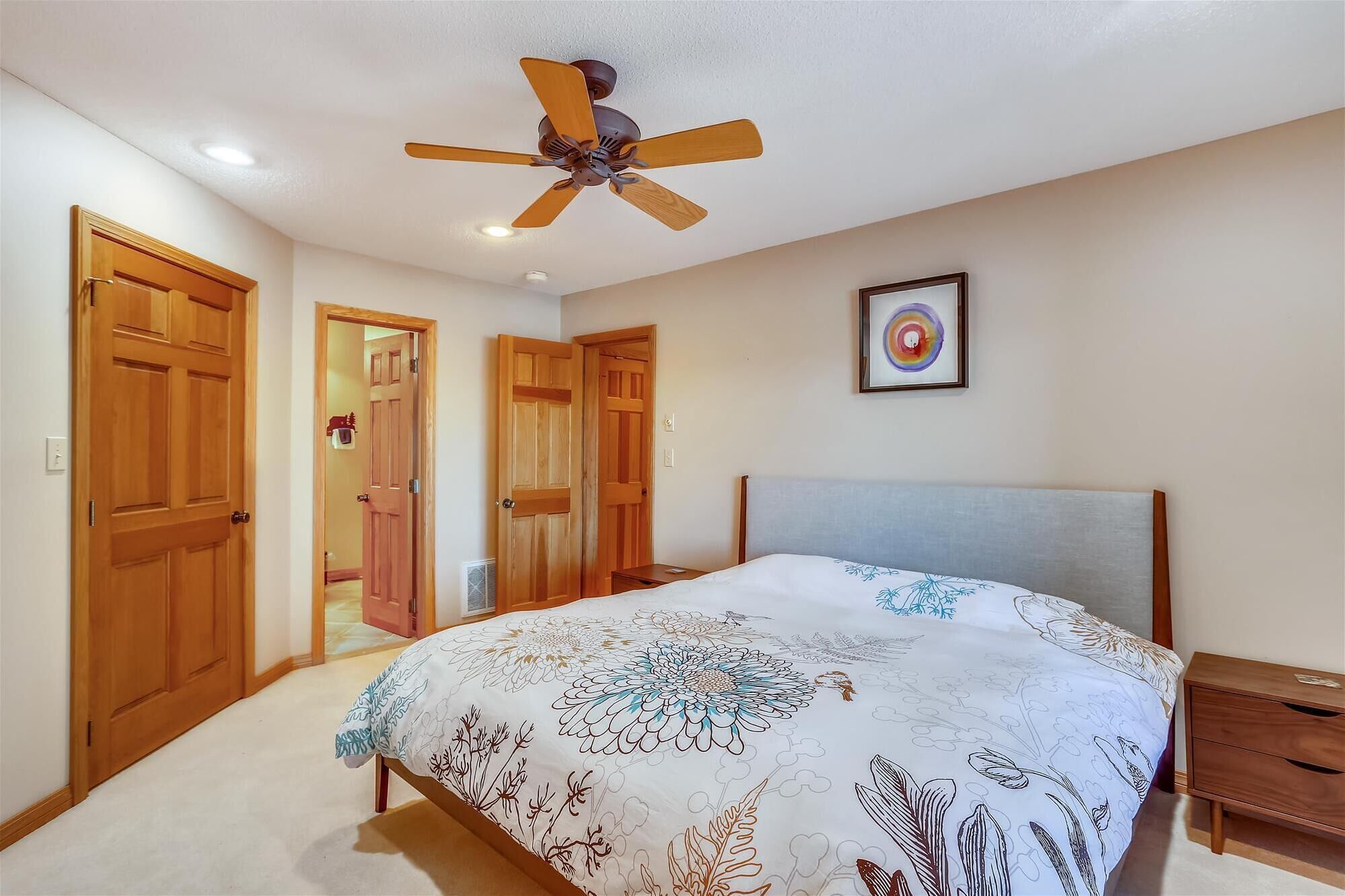 Une chambre à coucher avec un lit, un ventilateur de plafond, des portes en bois et un tableau encadré au mur.