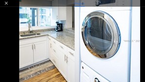 Une cuisine moderne avec des meubles blancs, un plan de travail en granit et un lave-linge encastré.