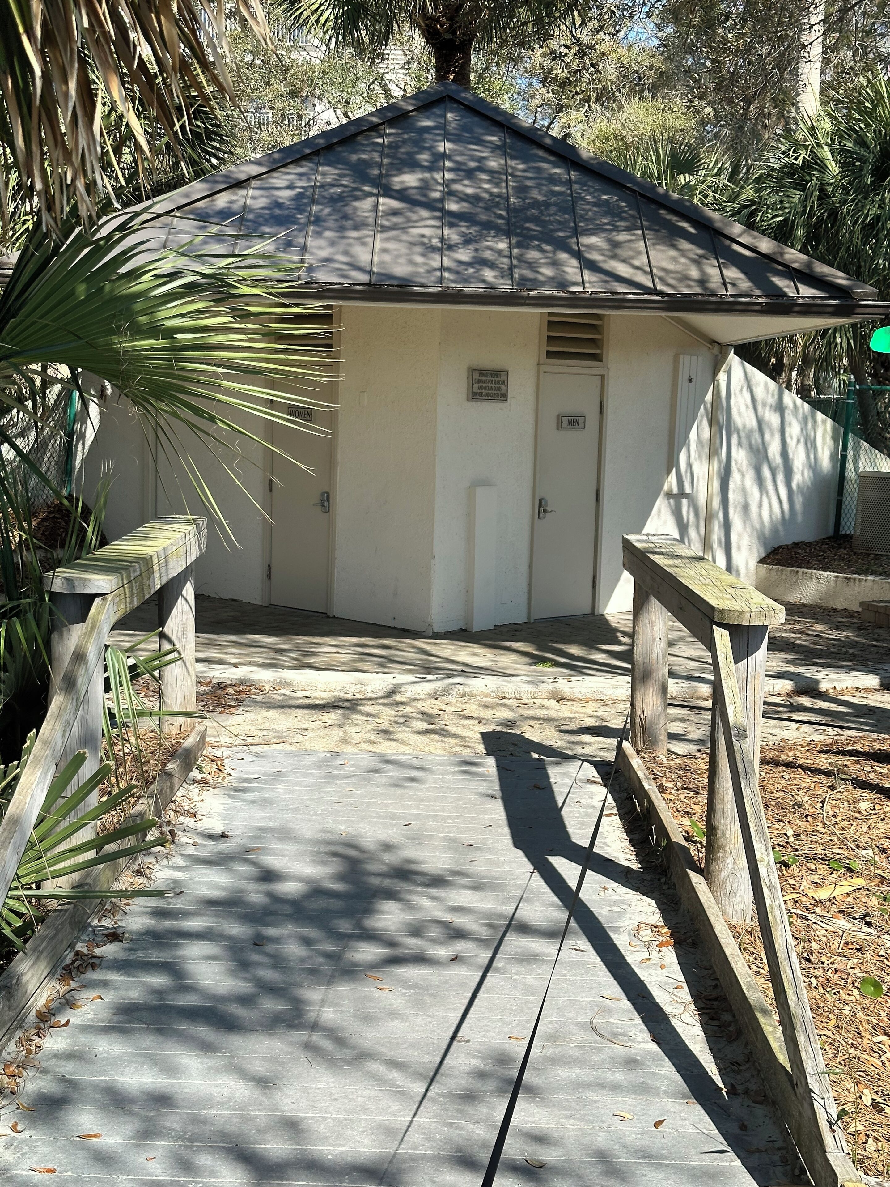 A small, white building with a dark roof, a door labeled "MEN," and a sign above the door.