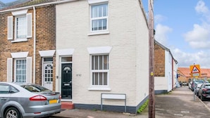 A two-story residential building with a black door and white shutters, a parked car, and a school crossing sign in the background. - Coal Miners Cottage - Moments to Seafront & Deal Town (Deal)