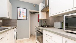 A modern kitchen with white cabinets, a stainless steel range hood, a microwave, and a gas stove. - Coal Miners Cottage - Moments to Seafront & Deal Town (Deal)