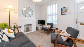 A modern living room with a fireplace, comfortable seating, a television, and a large window. - Coal Miners Cottage - Moments to Seafront & Deal Town (Deal)