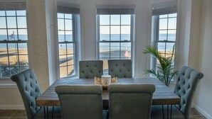 A dining area with a view of the beach, featuring a wooden table and four upholstered chairs.