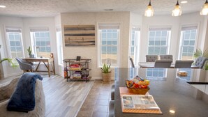 A spacious living room with a large island, a dining area, and a view of the ocean through large windows.