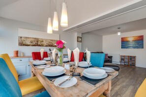 A dining area with a wooden table set for four, a vase with flowers, and a painting on the wall.