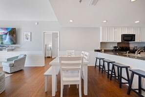 A modern kitchen with white cabinets, a black microwave, and a wooden dining table with four chairs. - This Beachfront Beauty is Calling! Oceanfront! Private Grill! Walk2PierPark! (Panama City Beach)