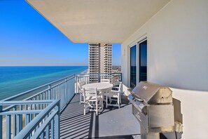 A balcony with a table and chairs, a grill, and a view of the ocean and buildings. - This Beachfront Beauty is Calling! Oceanfront! Private Grill! Walk2PierPark! (Panama City Beach)