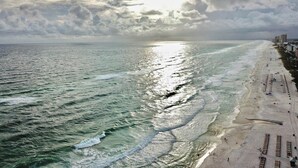 Uma praia com ondas, areal e edifícios ao fundo.