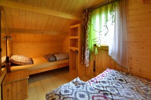 A wooden cabin room with a bunk bed, a small table, and a window with curtains.