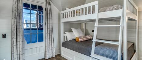 Dormitorio con literas, ventana, cortinas y vista a una casa.