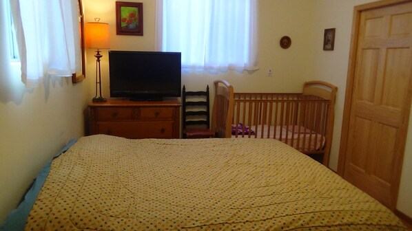 Un dormitorio con cama, televisión, cuna y cómoda.