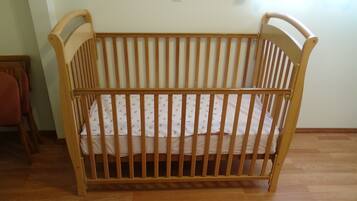 A wooden crib with a mattress and a pillow, positioned in a room with wooden flooring and a plain wall.