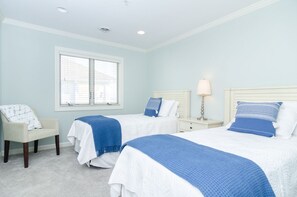 Une chambre avec deux lits, une chaise, une table de chevet et une lampe.