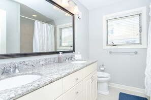 Une salle de bain avec deux lavabos, des toilettes, une fenêtre avec des stores et un miroir avec éclairage intégré.