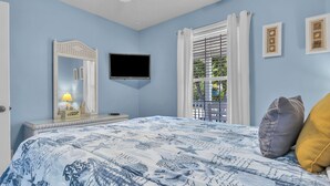 Ein Schlafzimmer mit einem Bett, einem Fernseher, einem Spiegel, einem Fenster mit Jalousien und einem Nachttisch mit einer Lampe.