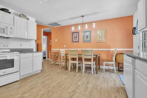 Une cuisine avec des meubles blancs, un four à micro-ondes et une cuisinière. On y trouve également un coin repas avec des chaises et une table en bois.