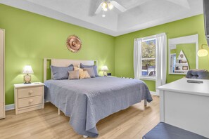 Une chambre à coucher avec un lit, des tables de chevet, un bureau et une fenêtre avec des rideaux.