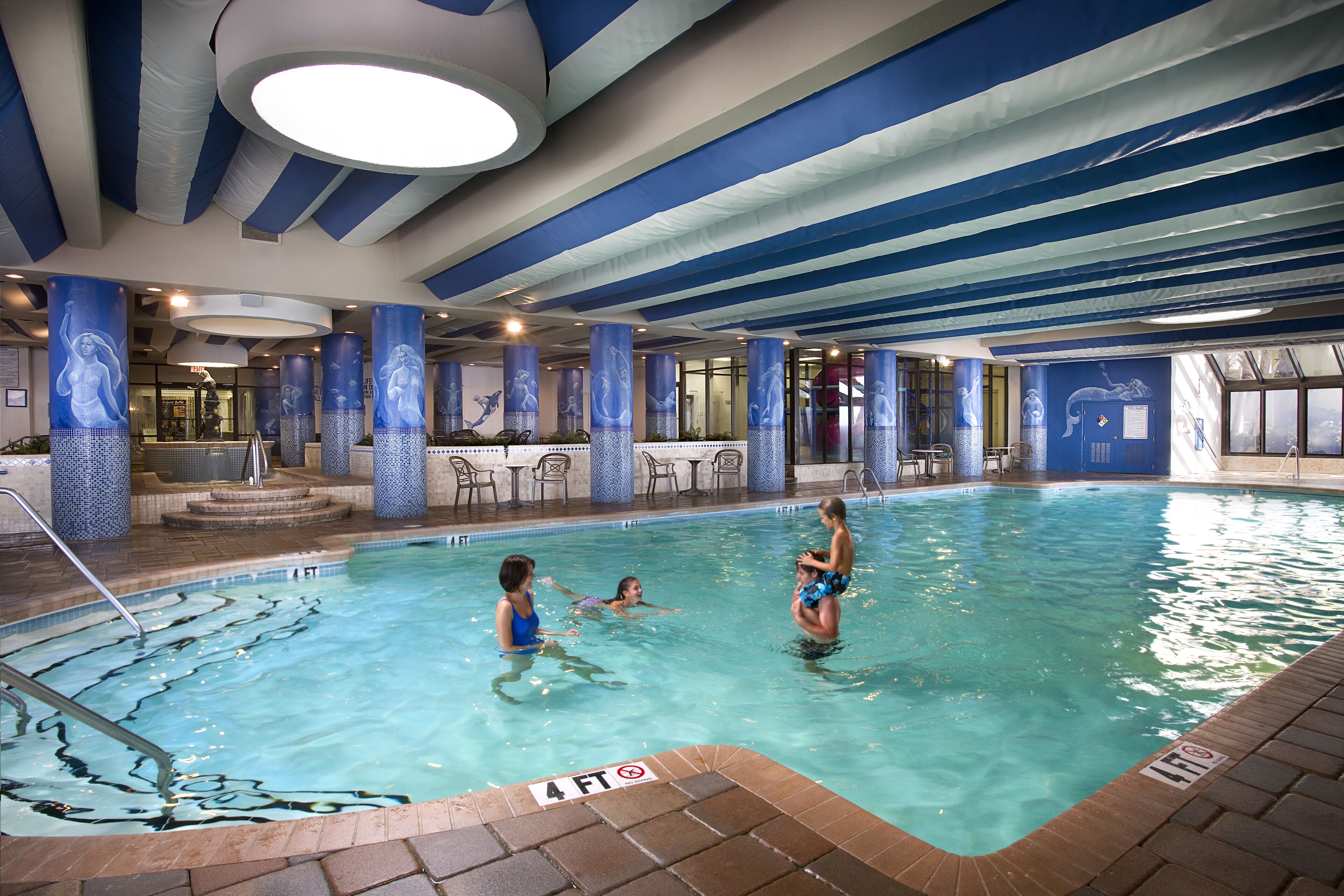 En inomhuspool med klart vatten, en markering som visar ett djup på 1,2 meter och ett tak med blåa ränder.