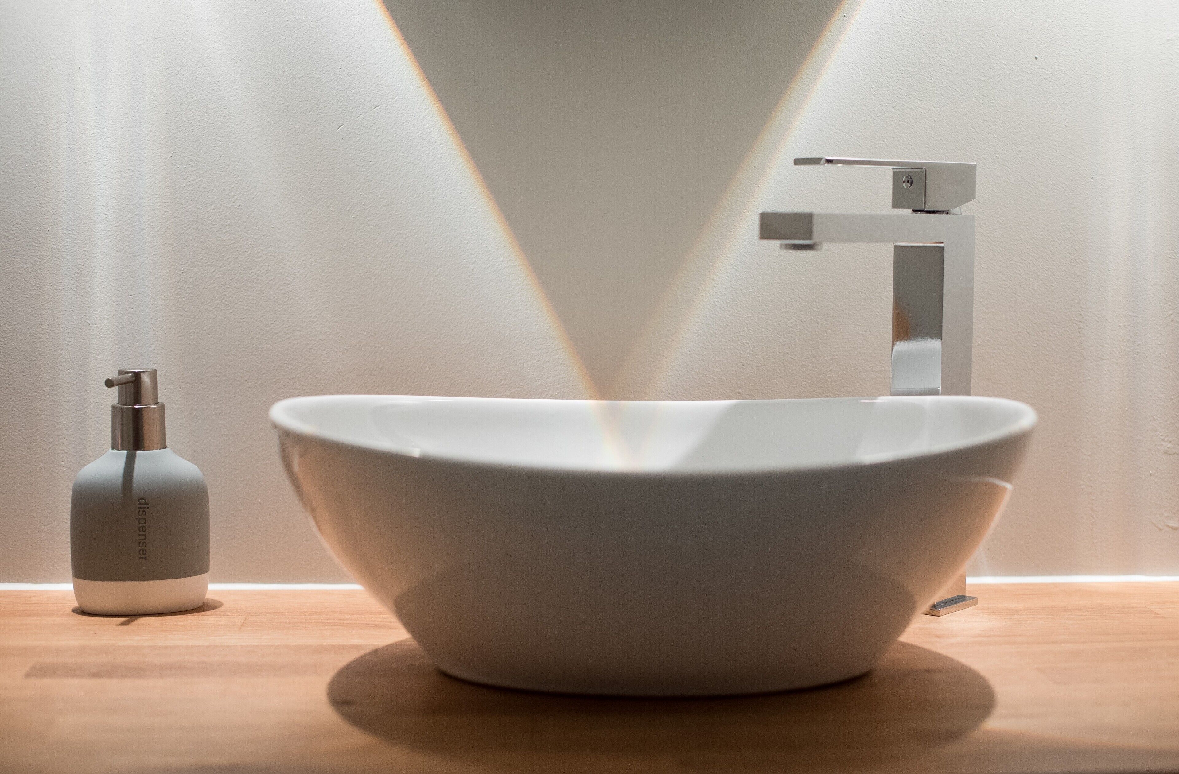 A modern bathroom with a white sink, a faucet, and a soap dispenser on a wooden countertop.