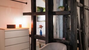 Una habitación moderna con techo de madera, cómoda blanca, sillón gris y una ventana grande con cortinas.