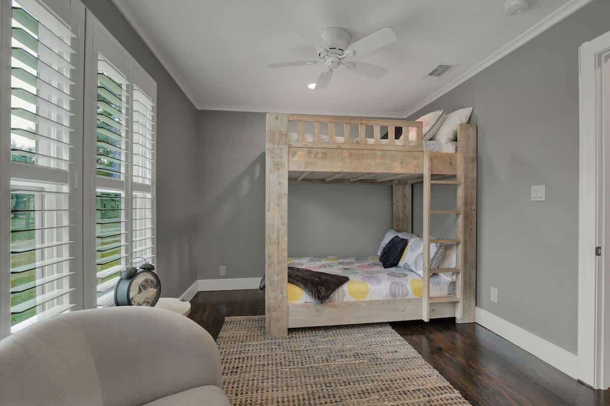 A room with a bunk bed, a ceiling fan, a window with blinds, and a rug on the floor.