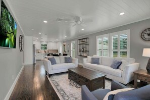 A spacious living room with a white sofa set, a coffee table, and a large painting on the wall.